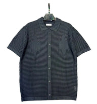 Dark gray knitted shirt on a hanger against a textured gray background
